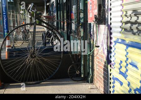 Antica bicicletta a ruota alta su una strada di Manhattan, adiacente ad un negozio di biciclette Foto Stock