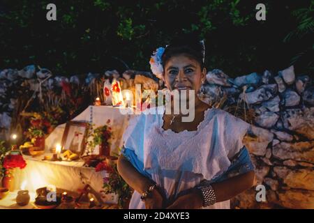 Merida, Messico - 31 ottobre 2018: Donna messicana in abiti tradizionali davanti all'altare con offerte per il giorno dei morti 'Dia de los muertos', Meri Foto Stock