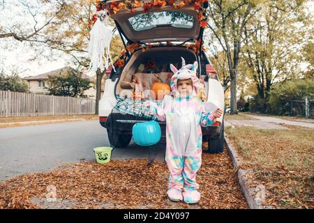 Trucco o tronco. Triste bambino sconvolto in costume unicorno che celebra Halloween in tronco di auto. Carino bimbo che si prepara per le vacanze all'aperto di ottobre. Sociale di Foto Stock
