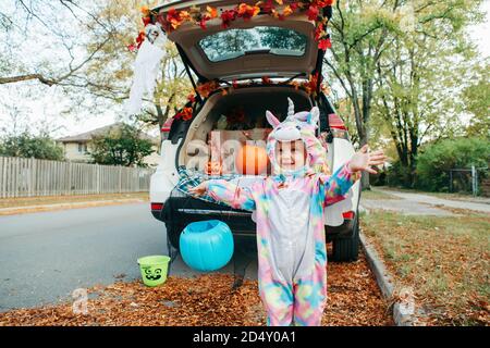 Trucco o tronco. Bambino felice in costume unicorno che celebra Halloween in tronco di auto. Carino bambino sorridente che si prepara per le vacanze di ottobre all'aperto. Socia Foto Stock