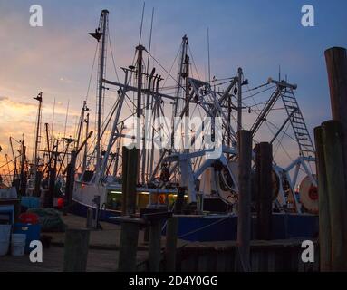 Le barche da pesca sono ormeggiate in un molo con la loro manipolazione in una silhouette parziale contro un cielo crepuscolo subito dopo il tramonto. Foto Stock