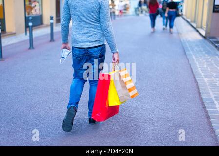 uomo solo a piedi nel centro della città con carta per lo shopping borse e una maschera facciale durante il venerdì nero sales.concept circa consumismo e nuova normalità Foto Stock
