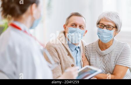 Medico e coppia senior che indossano maschere durante il coronavirus e l'epidemia di influenza. Protezione antivirus, quarantena domestica. COVID-2019. Assumere maschere. Foto Stock