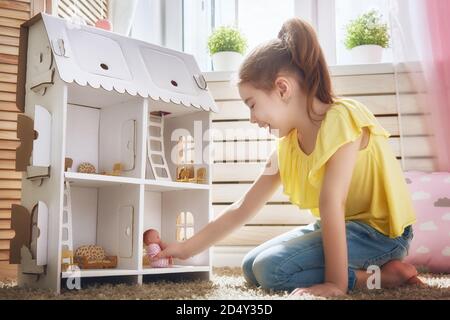 La ragazza felice gioca con la casa della bambola e l'orso del teddy a casa. Divertente, il bambino adorabile si diverte nella camera dei bambini. Foto Stock