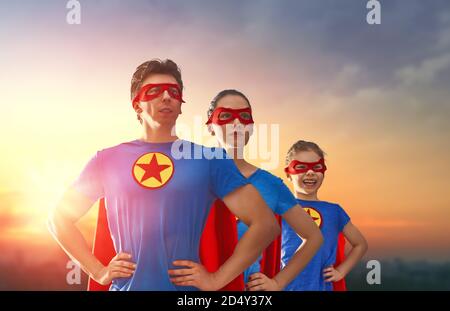 Madre, padre e loro figlia giocano all'aperto. Mamma, papà e bambina in costumi di un Supereroe. Concetto di super famiglia. Foto Stock