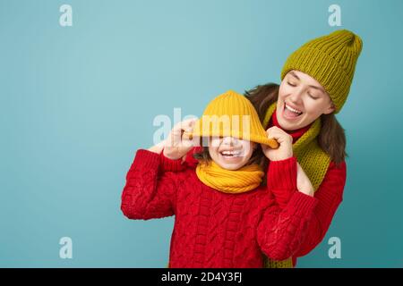 Ritratto invernale di famiglia felice e amorevole che indossa cappelli, snodi e pullover in maglia. Madre e bambina che si divertono, giocando e ridendo sul dorso del tepal Foto Stock