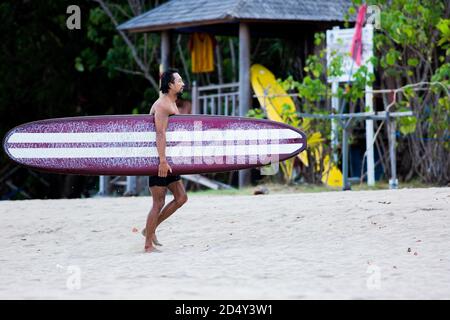 un uomo che cammina sulla spiaggia con un longboard.. di alta qualità foto Foto Stock