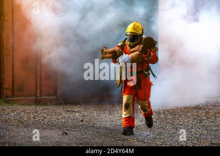 Soccorso dei vigili del fuoco, Fireman che esce dalla costruzione in fiamme e tiene un bambino tra le sue braccia da un incidente di fuoco. Foto Stock