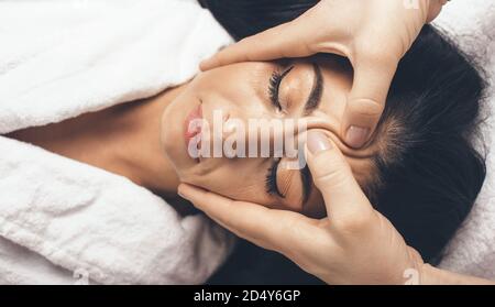 Donna con brunette che ha un massaggio viso anti invecchiamento presso la spa salone mentre si sdraiano con gli occhi chiusi Foto Stock