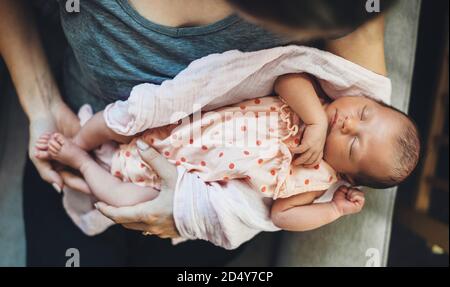 Donna caucasica che tiene in mano la figlia appena nata che dorme in un bel vestito Foto Stock