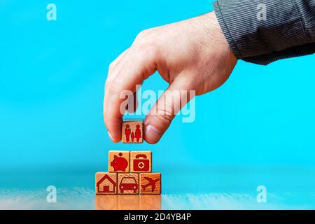 Le mani di un uomo tiene un cubo tra le mani e costruisce una piramide. Sicurezza e assicurazione: Auto, immobiliare e immobiliare, viaggi, Finanza, Salute, Fami Foto Stock