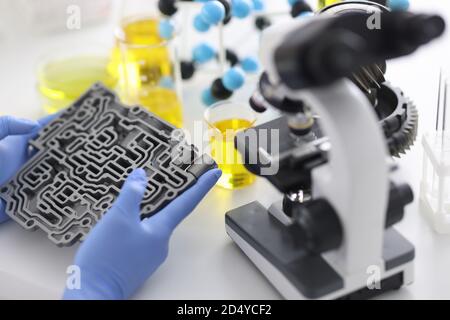 La trasmissione automatica giace in guanti di gomma su tavolo con microscopio e provette in closeup di laboratorio chimico Foto Stock