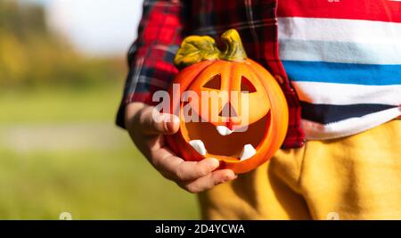 Mano del capretto che tiene la lampada della zucca di Jack'o, trucco o trucco il giorno di Halloween. Concetto per le vacanze autunnali background. Foto Stock