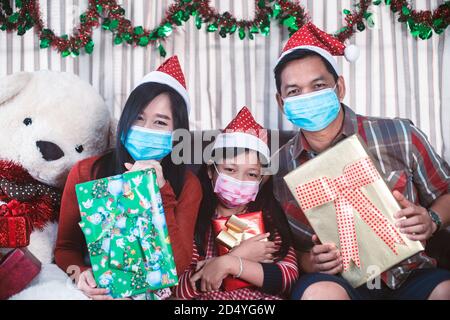 Famiglia asiatica in interior.Happy natale padre e figlia che indossa faccia la maschera e tenendo una scatola del regalo con il sorriso Foto Stock
