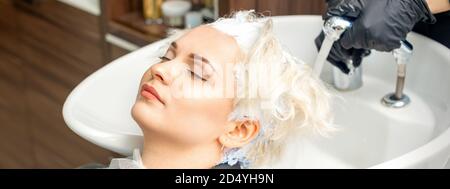 Parrucchiere preparatevi a lavare via la tintura bianca dai capelli di giovane donna caucasica in lavello al salone di bellezza Foto Stock