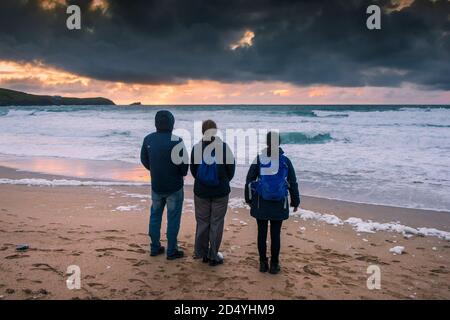 Una famiglia di vacanzieri che si trova sulla Fistral Beach guardando uno spettacolare tramonto a Newquay in Cornovaglia. Foto Stock