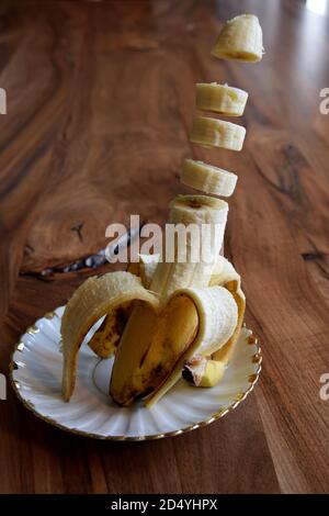 Fette di banana che lavano sopra un piatto su un tavolo di legno. Banana levitazione. Foto Stock