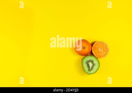 Tangerina intera, mezza tangerina e mezzo kiwi isolato su sfondo giallo Foto Stock