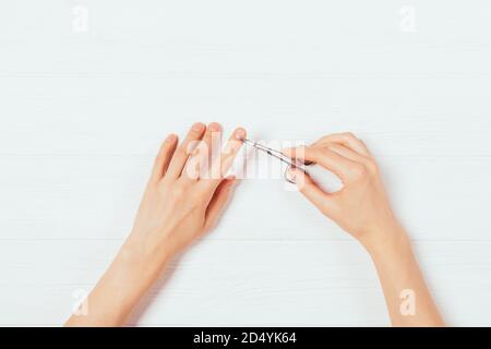 Vista dall'alto delle mani femminili che tagliano la cuticola con forbici per manicure sul tavolo bianco. Foto Stock