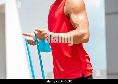 Uomo atletico muscolare senza volto facendo esercizio di curl bicep con resistenza banda all'aperto Foto Stock