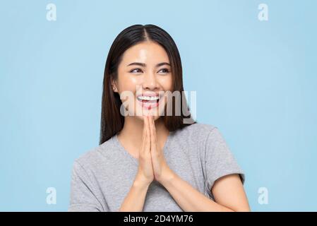 Sorridente bella donna asiatica facendo gesto Wai per il saluto o. grazie isolato su sfondo azzurro Foto Stock