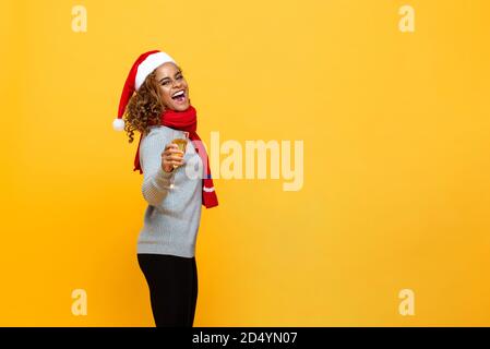Sorridente donna afroamericana felice che indossa abiti di Natale con champagne vetro in mano celebrante vacanza su sfondo giallo isolato con copia Foto Stock