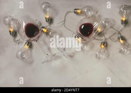 Due bicchieri di vino rosso e retrò ghirlanda di Natale con le lampade accese su marmo bianco dello sfondo. Laici piana, spazio Foto Stock