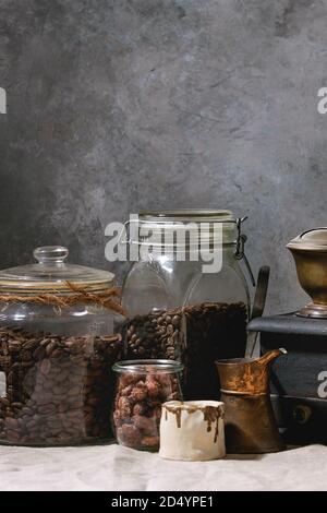La raccolta del caffè. Nero arrosto i chicchi di caffè in barattolo, vintage macinino da caffè, jezve pot, crema brocca, dolci di mandorle zuccherata in piedi sulla tavola di biancheria da letto e da bagno Foto Stock