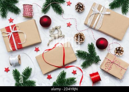 Scatole regalo artigianali natalizie, ramo d'albero, baubles, cono di pino, stelle e renne su sfondo marmoreo, posa piatta. Regali di Natale Foto Stock