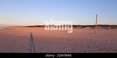 Il tramonto illumina il cielo sull'isola tedesca di wangerooge. La lunga ombra del fotografo è visibile Foto Stock