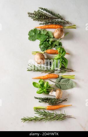 Varietà di cucina fresca erbe con mini carote e funghi champignon in fila su marmo bianco dello sfondo. Appartamento laico, spazio. Concetto di cucina a vista, cibo Foto Stock