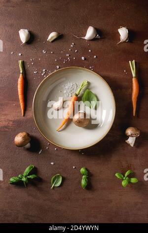 Il basilico fresco erbe con mini carote e funghi champignon in fila e nella piastra su sfondo marrone. Appartamento laico, spazio. Concetto di cucina a vista, cibo backgro Foto Stock