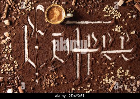 Iscrizione calligrafico lettere gotiche caffè sulla massa di caffè nero sparsi su marmo bianco. Arrosto e fagioli non torrefatto, tazza di espresso, spice Foto Stock