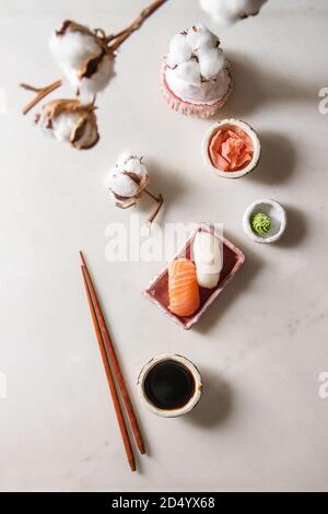 Set di sushi nigiri con salmone e butterfish in rosa di servizio in ceramica piastra, bastoncini, bocce di salsa di soia e zenzero sott'aceto, fiori di cotone su whi Foto Stock