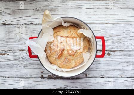 Vista dall'alto del pane artigianale appena sfornato in un forno olandese rosso. Piatto. Foto Stock