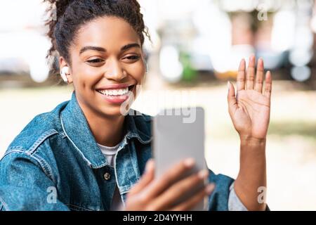 Donna africana con smartphone che effettua la videochiamata seduto in Park Foto Stock