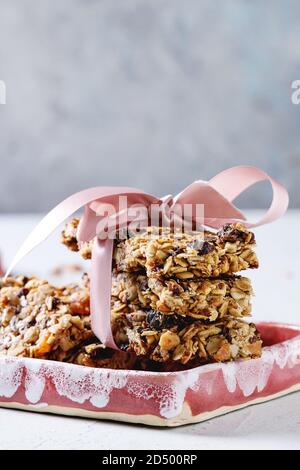 Energia in casa di avena granola bar con frutta secca e noci intere e rotto con nastro rosa in piatti di ceramica sulla tabella grigia. Snack sani. Foto Stock