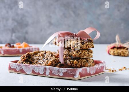 Energia in casa di avena granola bar con frutta secca e noci intere e rotto con nastro rosa in piatti di ceramica sulla tabella grigia. Snack sani. Foto Stock