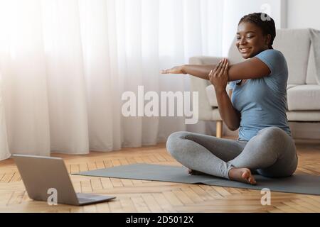 Donna africana allegra che si allunga davanti al laptop, facendo allenamento a casa Foto Stock