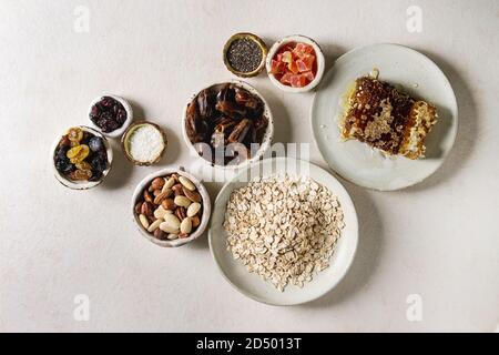 Varietà di frutta secca, noci, miele e fiocchi di avena in ciotole di ceramica per la cottura in casa sana colazione muesli muesli o barrette energetiche su bianco t Foto Stock