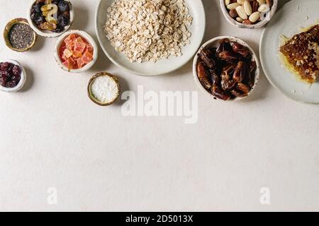 Varietà di frutta secca, noci, miele e fiocchi di avena in ciotole di ceramica per la cottura in casa sana colazione muesli muesli o barrette energetiche su bianco t Foto Stock