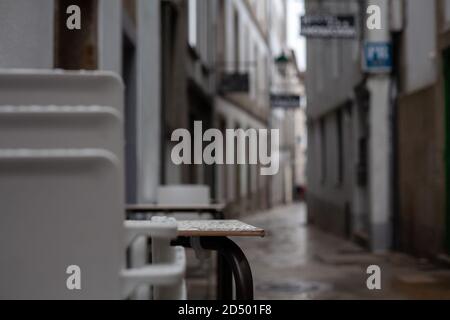 Sedie di plastica impilate da un ristorante outisde in una vecchia strada rustica piovosa di Santiago de Compostela, Spagna. Chiuso accatastato turismo spagna rustico. Foto Stock