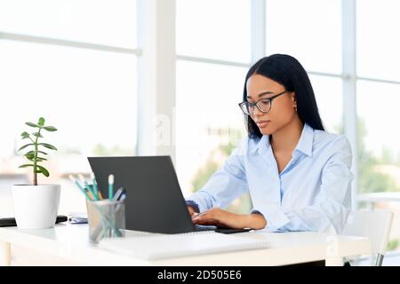 Giovane donna afroamericana di successo che usa e digita sul laptop in un ufficio moderno. Donna nel concetto di impresa Foto Stock