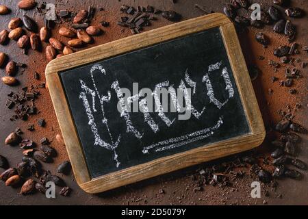 Varietà di fresco e secco Fave di cacao, cioccolato fondente tritato e lavagna con iscrizione calligrafica gotica scritte a mano lettere Choco oltre il coc Foto Stock