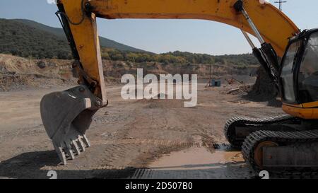 Macchina movimento terra per scavo e scarico. Terreno sabbioso e verde collina di montagna sullo sfondo. Foto Stock