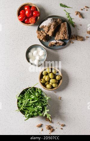 Mozzarella, pomodorini e olive antipasto antipasti servita in ciotole con foglie di rucola e pane di segale su grigio Sfondo texture. Laici piana, spazio Foto Stock