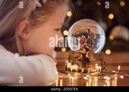 Ragazza che guarda una palla di vetro con una scena di La nascita di Gesù Cristo in una palla di vetro Un albero di Natale Foto Stock