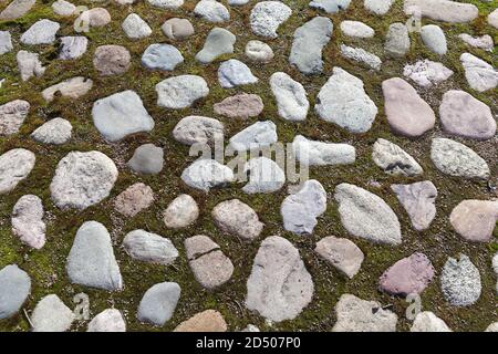 Antico pavimento in pietra di granito con muschio verde in spazi vuoti, vecchi ciottoli sfondo foto Foto Stock