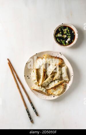 Fritti gnocchi asiatici Gyozas potstickers in bianco piastra ceramica servita con bacchette e una ciotola di soia Salsa di cipolla bianca su sfondo marmo. Appartamento Foto Stock