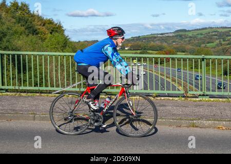 Ciclismo maschile equitazione specializzata sport bici da strada sulla strada di campagna che attraversa il ponte autostradale nel Lancashire rurale, Regno Unito Foto Stock